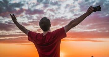 Un homme les bras ouvert devant un coucher de soleil